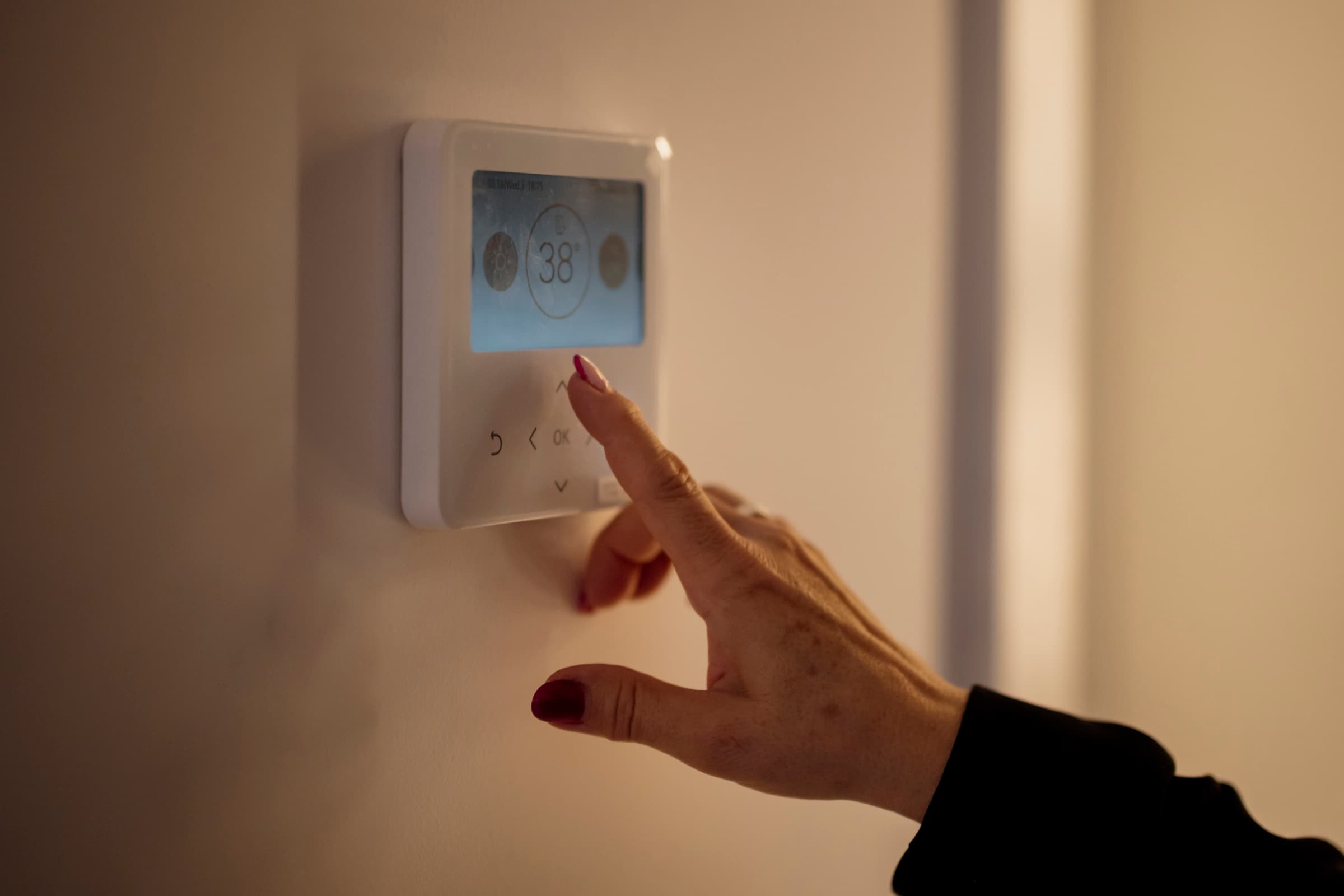 A hand adjusting a wall thermostat.