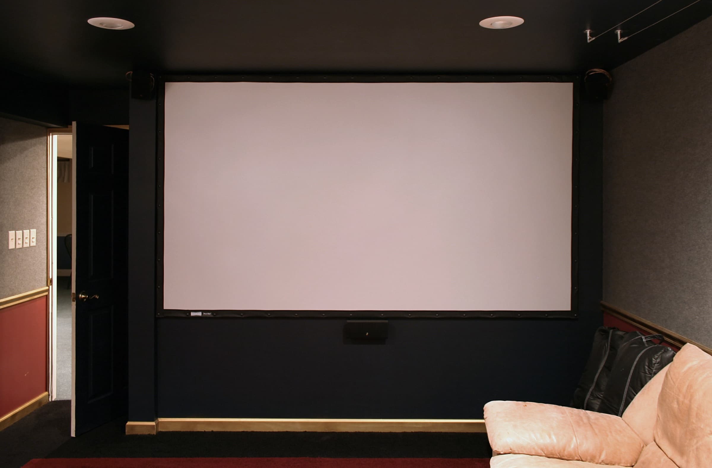 A basement home theater room with a large projection screen, recessed lighting and a leather sofa.