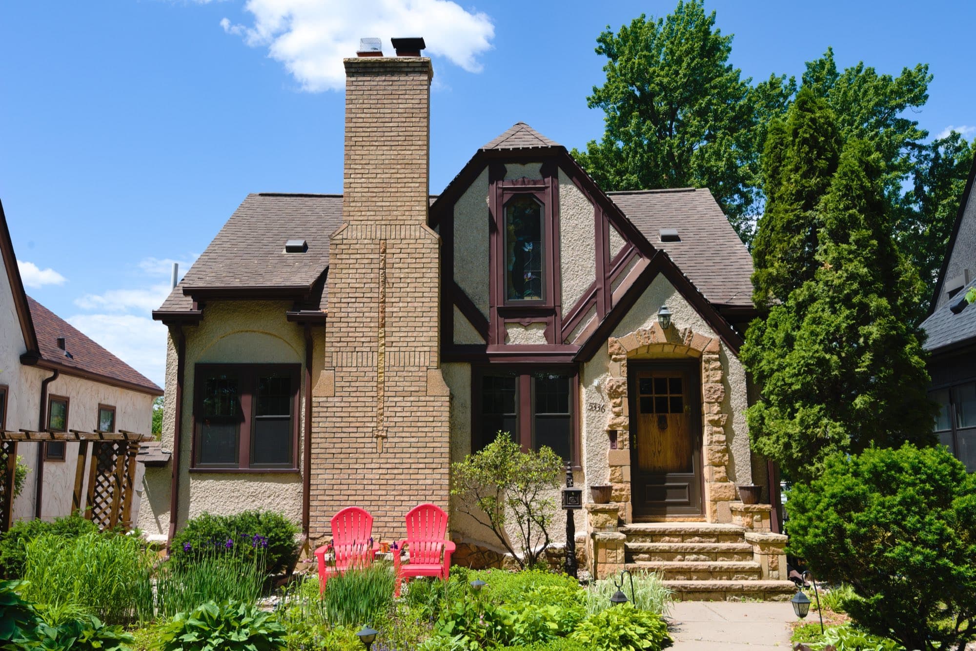 A two-story brick and stucco American house with a tall chimney, mature trees and a landscaped front yard.