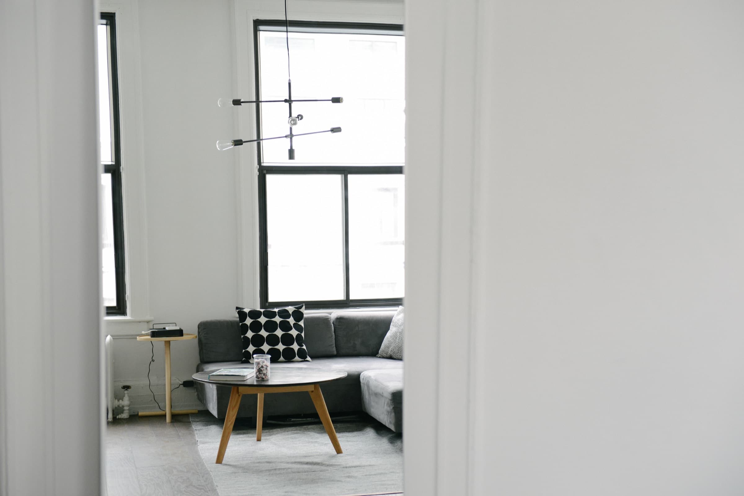 A bright loft living room with a gray sectional sofa and a black-and-white patterned pillow, seen through a doorway.