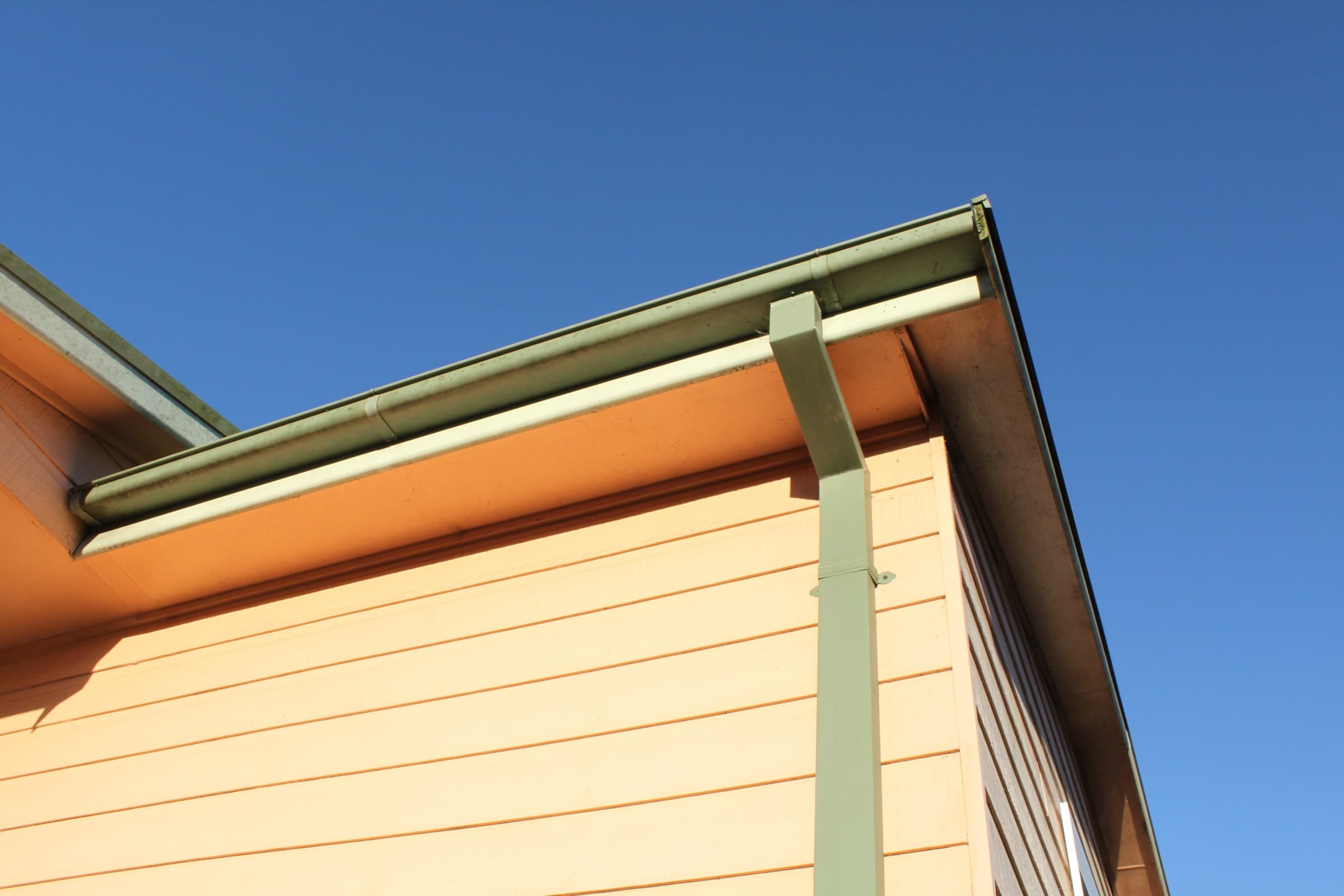 A rain gutter and downspout on a house, against a blue sky.